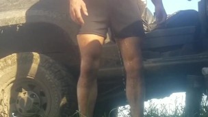 Grown man pees himself in shorts and bare feet outdoors in the grass by the dirty truck
