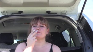 A cute bbw smokes in the street near the car