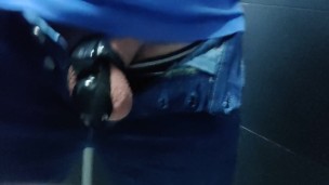 Locked in a chastity cage, man is pissing in a public toilet