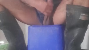 Crouches down on crate in boots and shorts, has a quick fiddle of that big uncut cock and balls