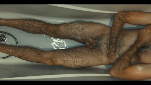 Hairy guy soaps up in bath, strokes, plays with his dick and foreskin and pisses on himself